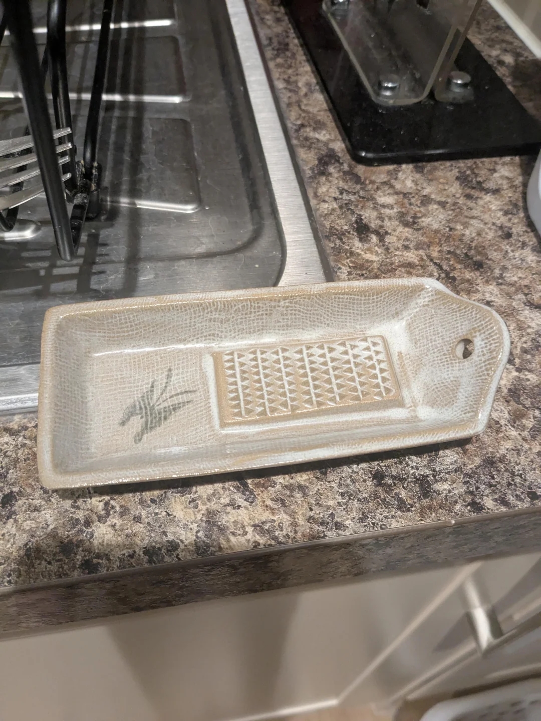 A ceramic gratin dish with a textured grating section sits by a kitchen sink, used for grating food items like garlic or ginger