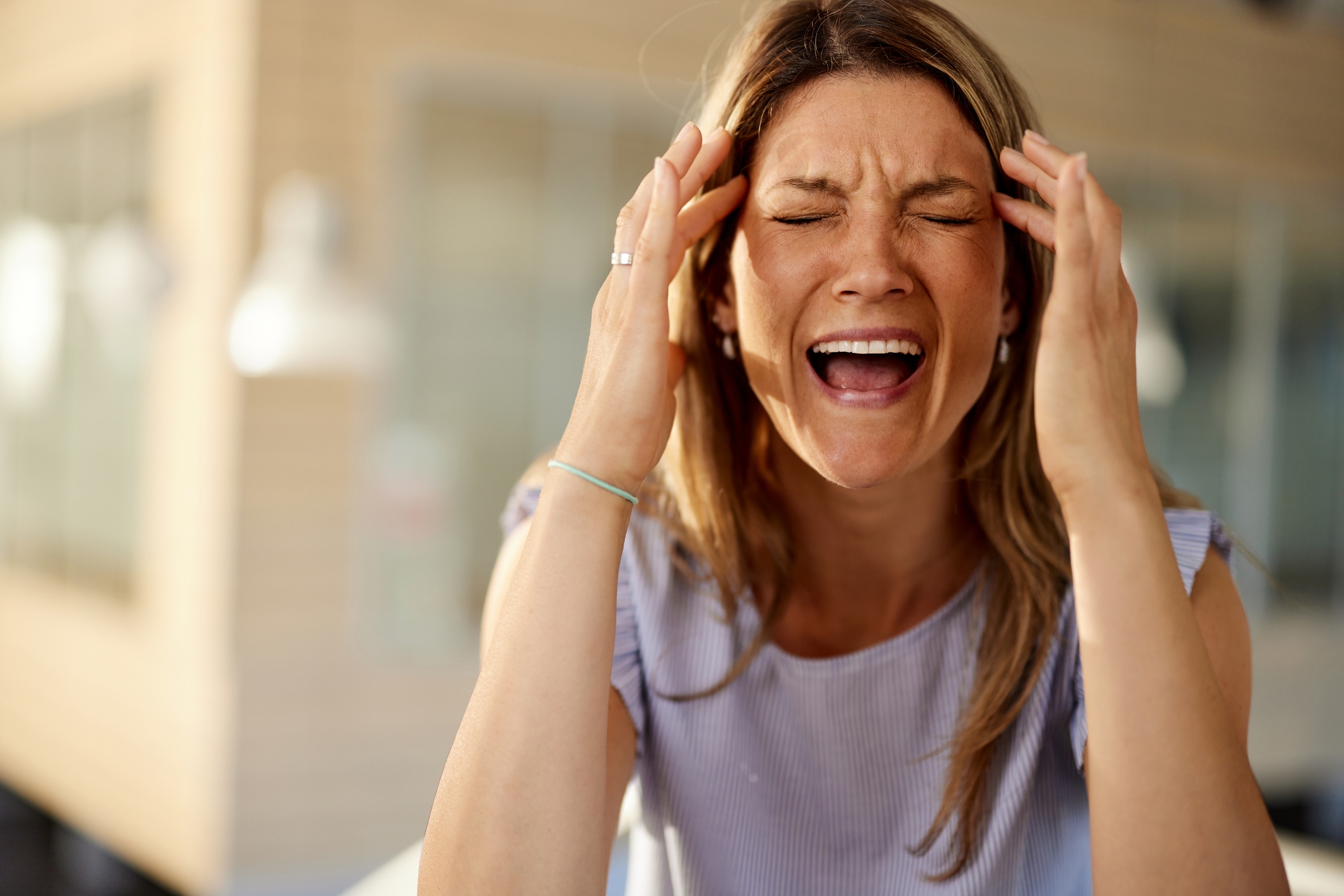 A woman indoors with a pained expression, touching her temples as if experiencing a headache