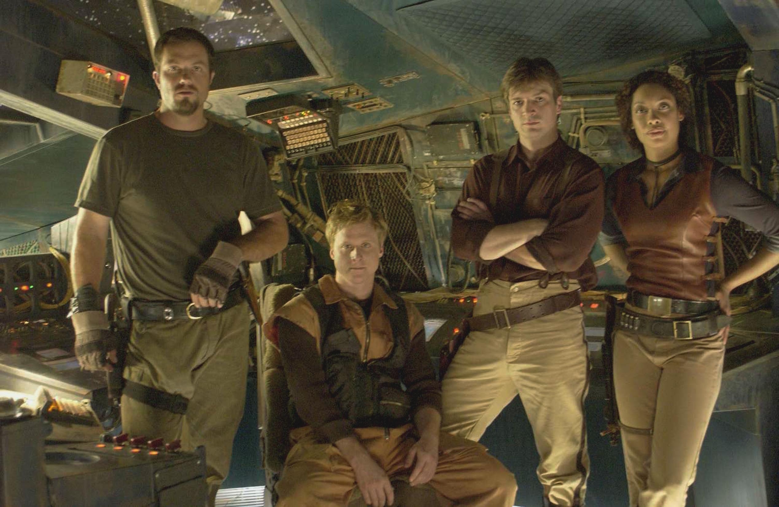 Group of four people posing in a futuristic spaceship set. They wear casual and rugged outfits, suggesting an adventurous or sci-fi theme