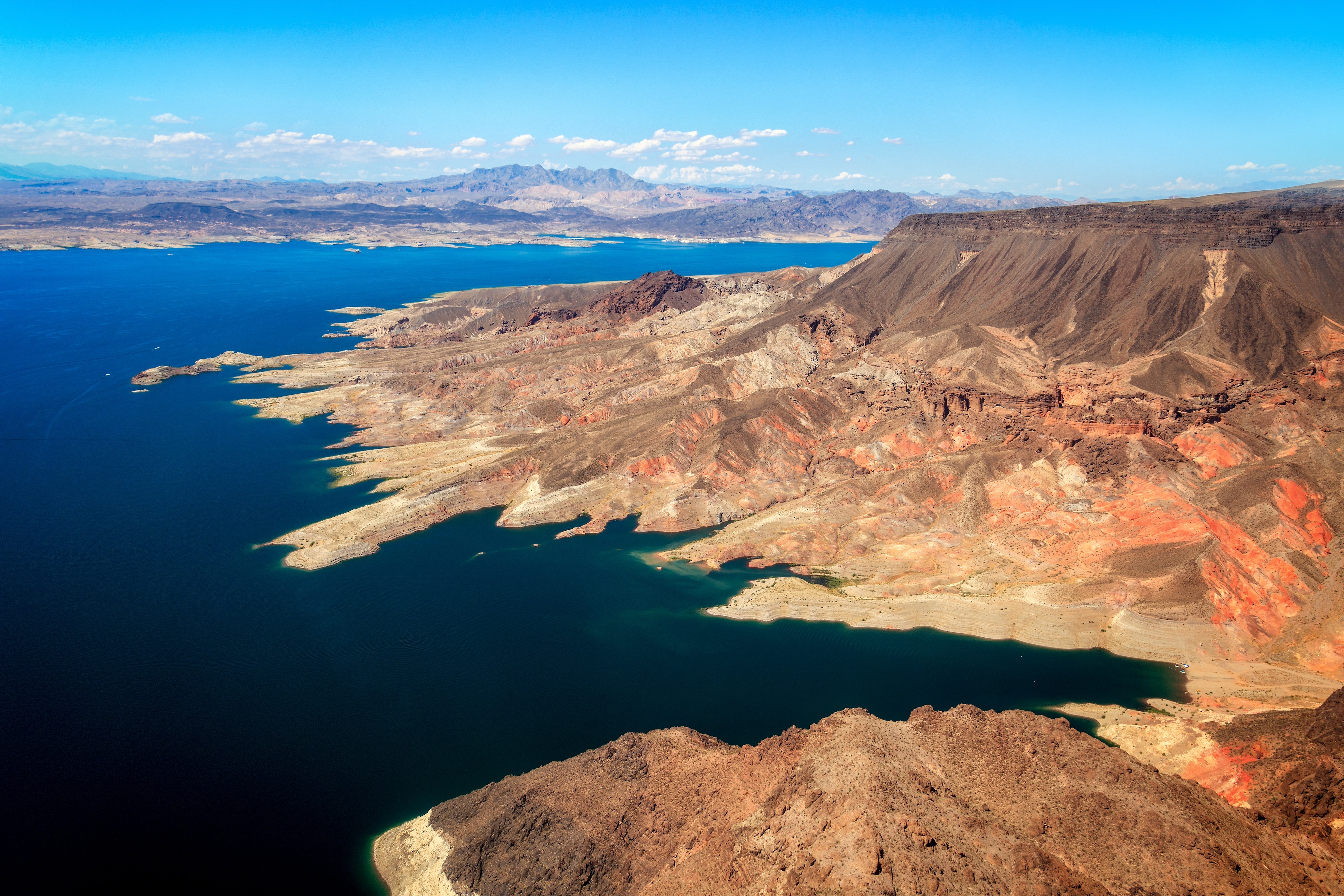 Aerial view of a vast desert landscape, showing rugged terrain and a large blue lake stretching into the distance, under an open sky