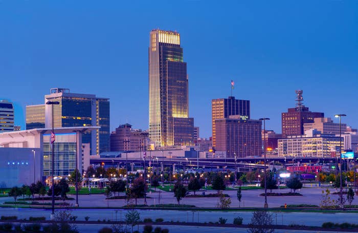 Cityscape featuring a tall, illuminated skyscraper dominating the skyline amid various buildings and empty parking areas at dusk