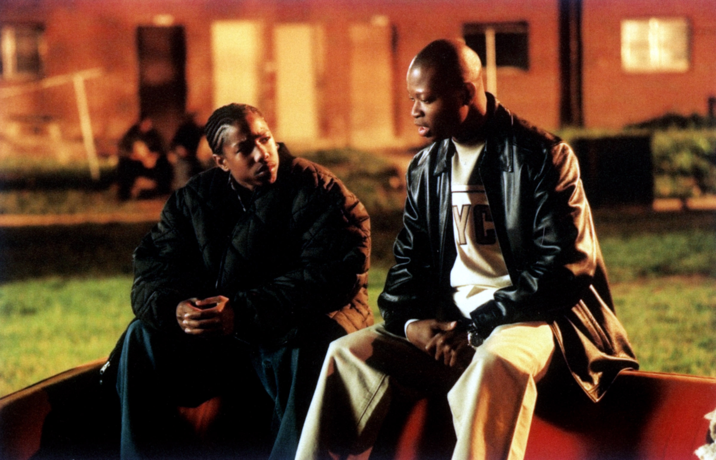 Two characters sit on a park bench, engaged in a serious conversation, in a scene from a TV or movie setting