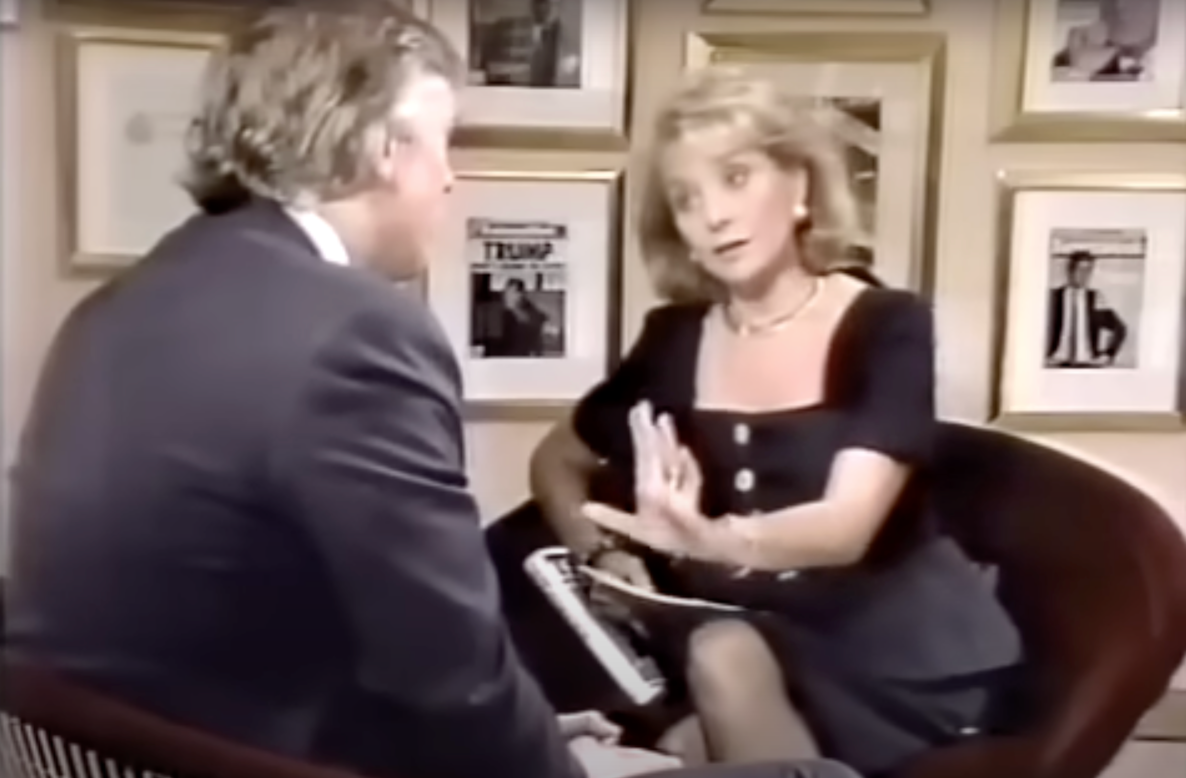 Two individuals sitting in chairs, engaged in a discussion, with magazine covers framed on the wall behind them