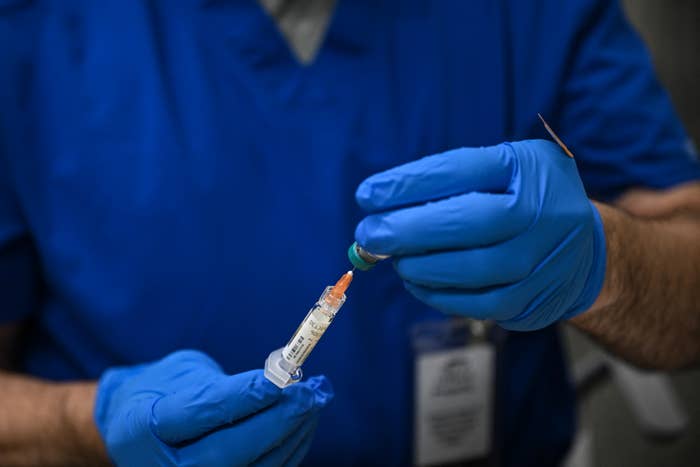 Person in blue gloves holding a syringe and needle, preparing it for a measles vaccine