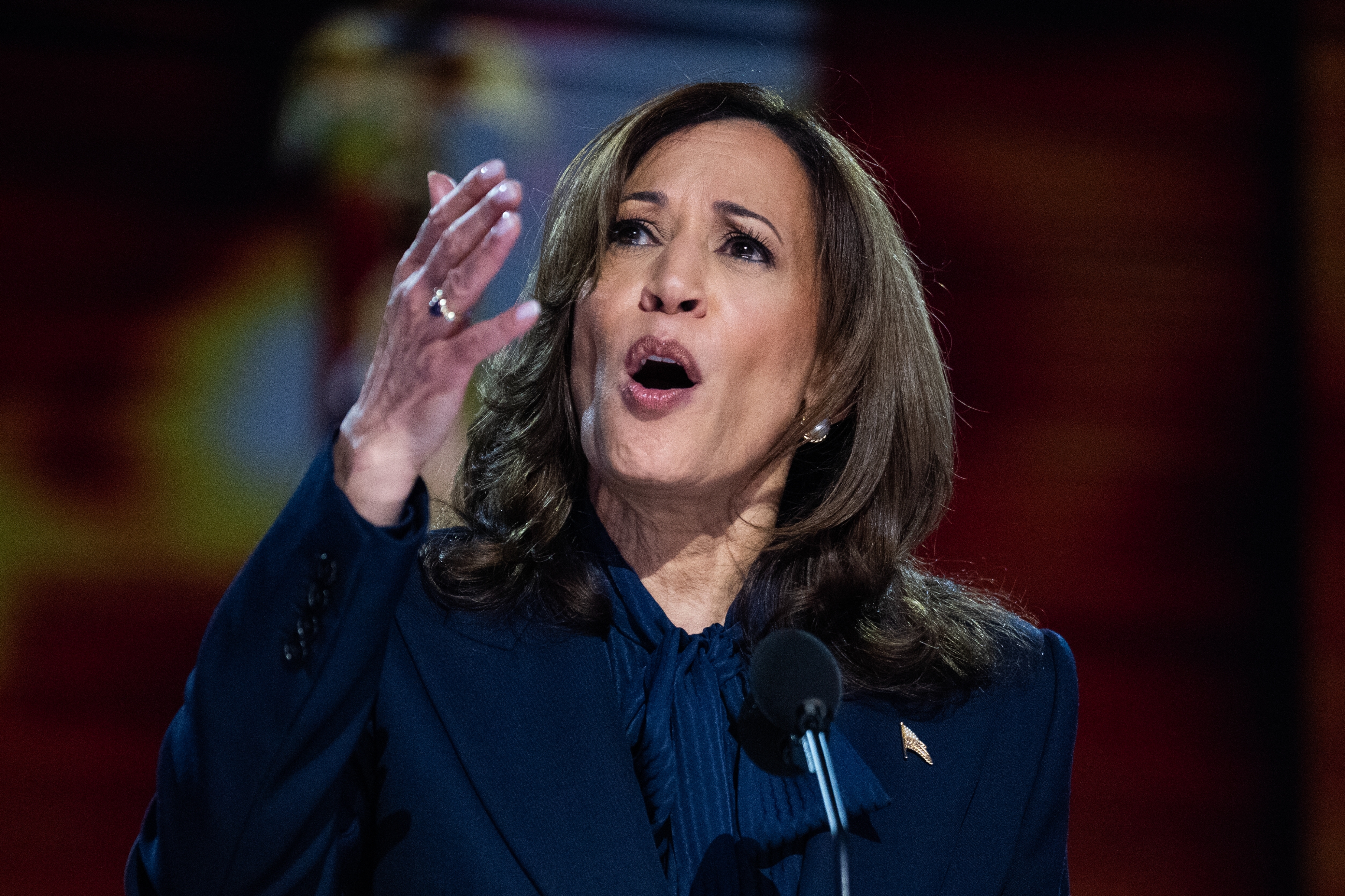 Kamala Harris in a suit is speaking passionately at a microphone, with her hand raised for emphasis