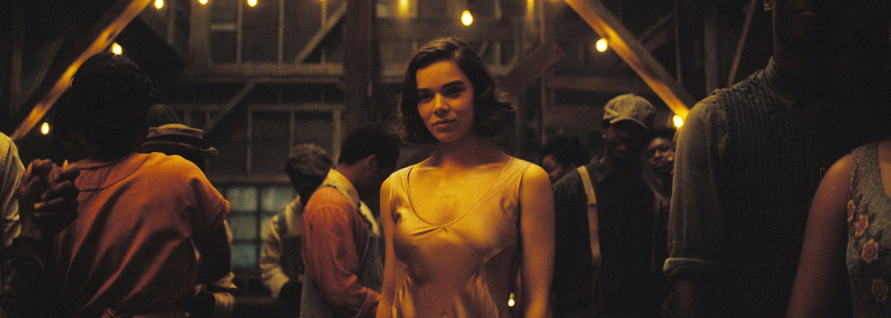 Person in an elegant dress stands alone at a dimly lit party, surrounded by groups in casual attire