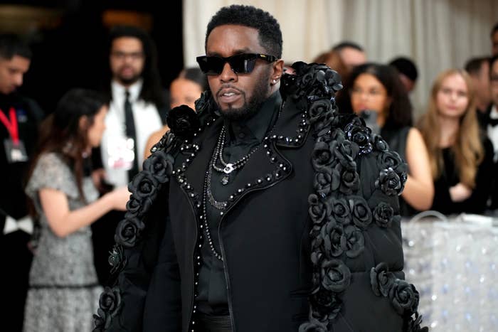 A person in an embellished coat adorned with floral designs and sunglasses attends an event