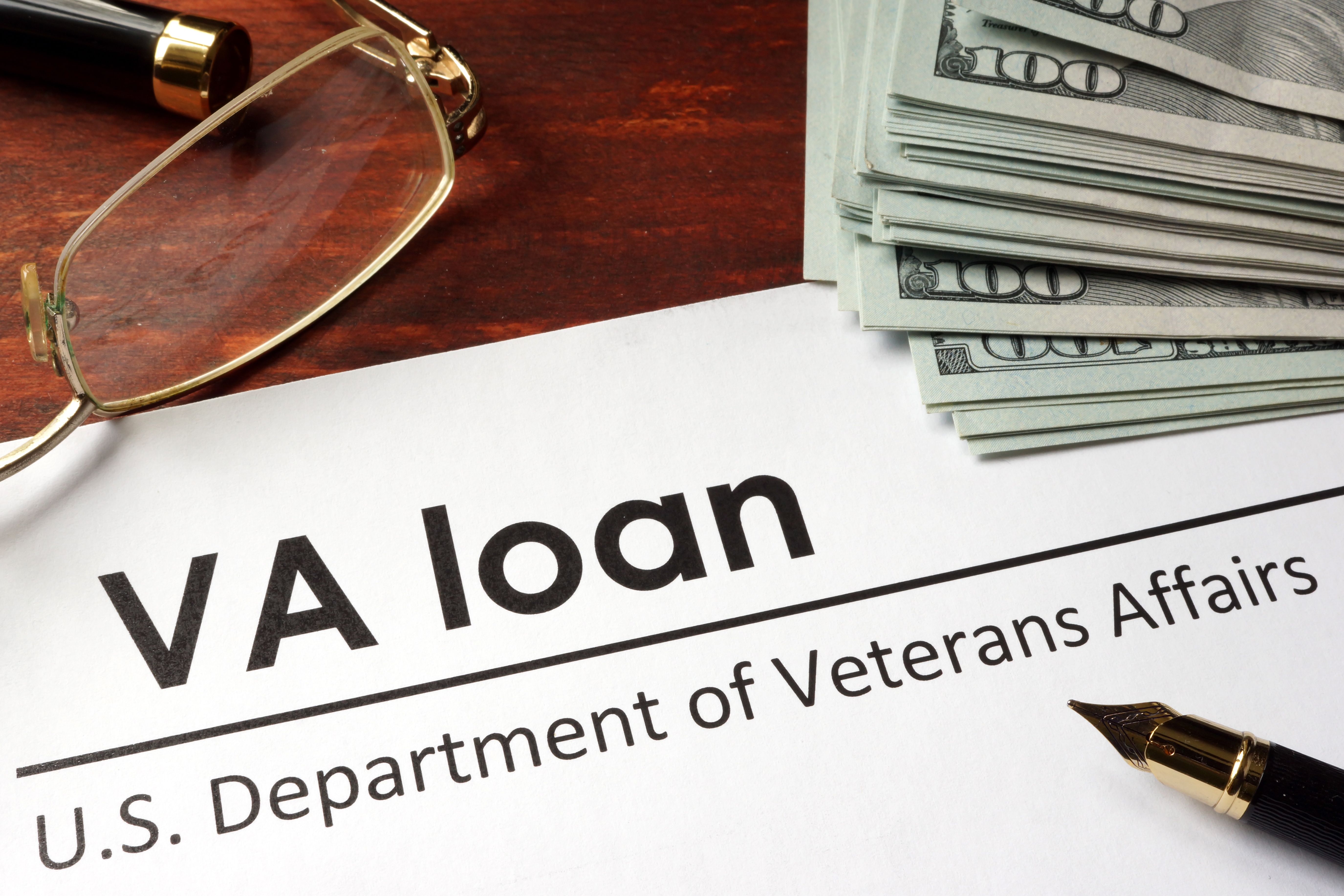 VA loan document with glasses and pen on a table beside a stack of $100 bills