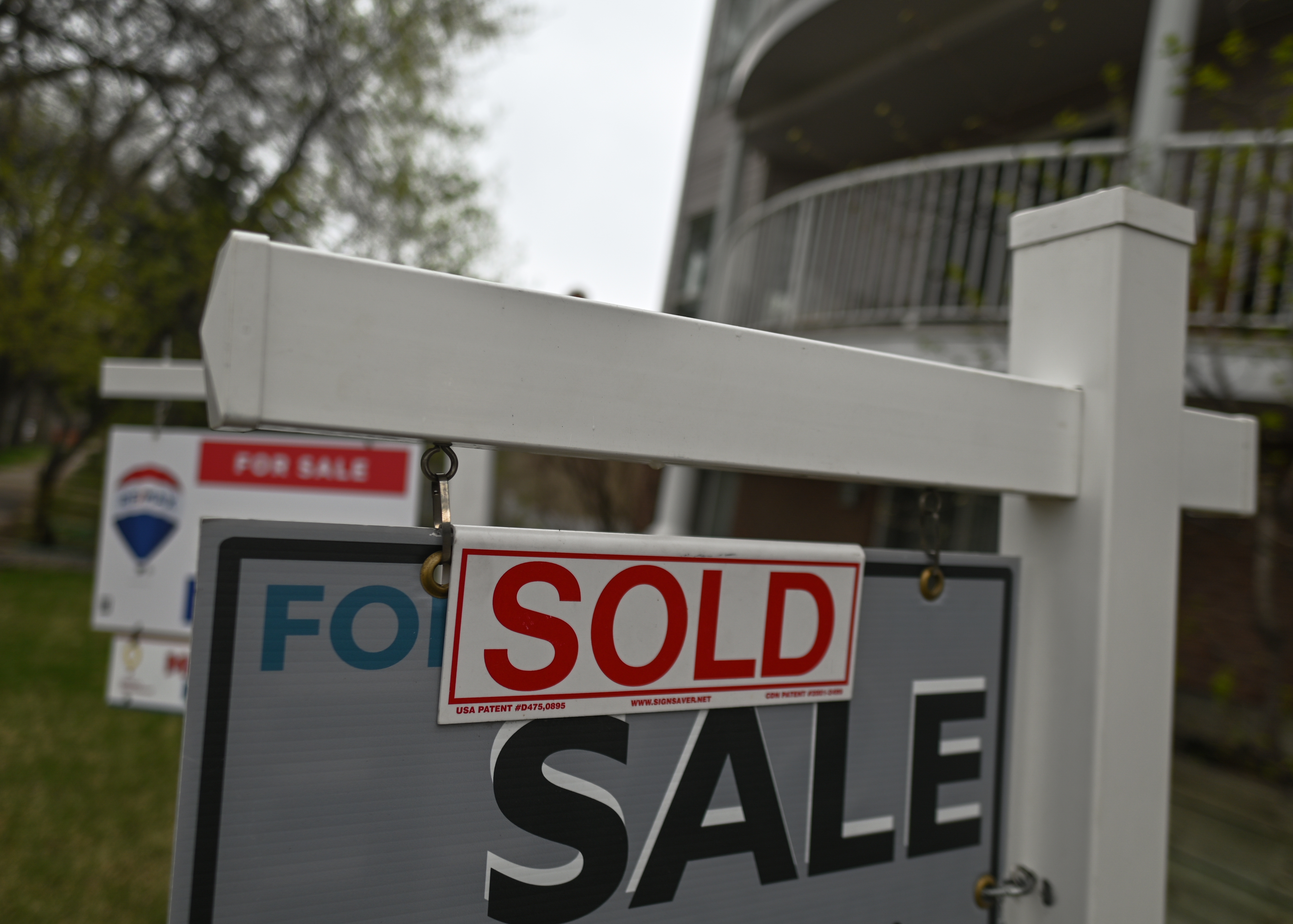 A "Sold" sign hangs on a real estate post in front of a residential building, indicating a closed property deal