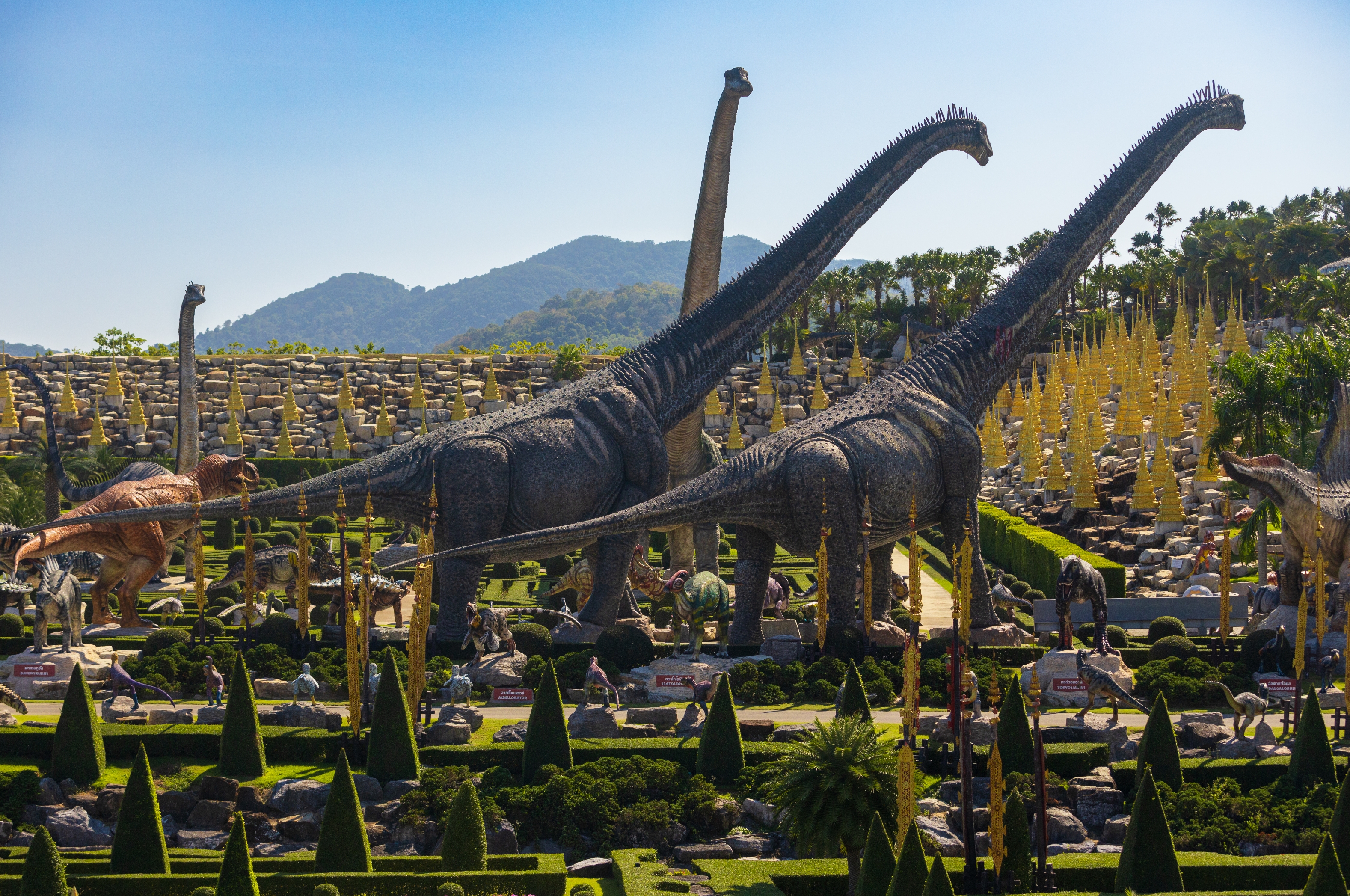 Large dinosaur statues in a landscaped park with mountains in the background