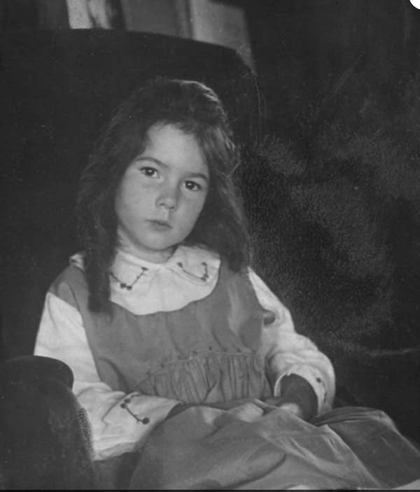 Vintage photo of a young girl with long hair sitting in an armchair, wearing a dress with a white collar and cuffs