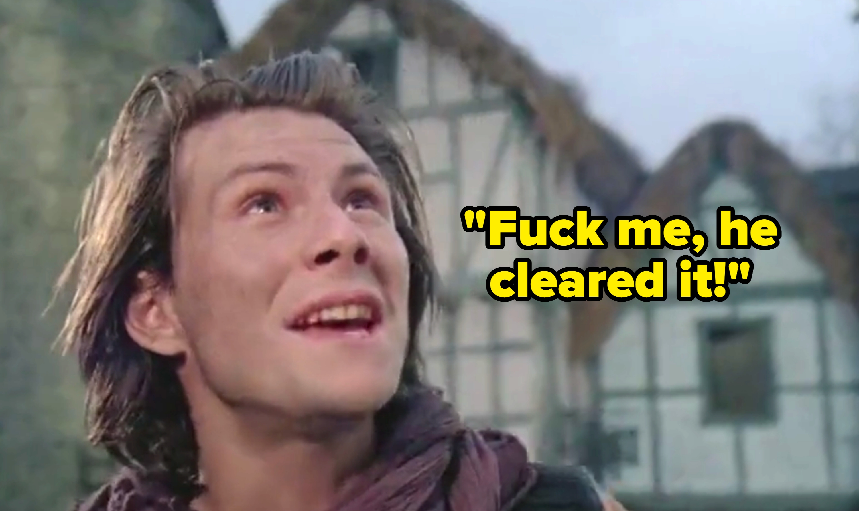 Person smiling, looking up in front of medieval-style buildings with thatched roofs