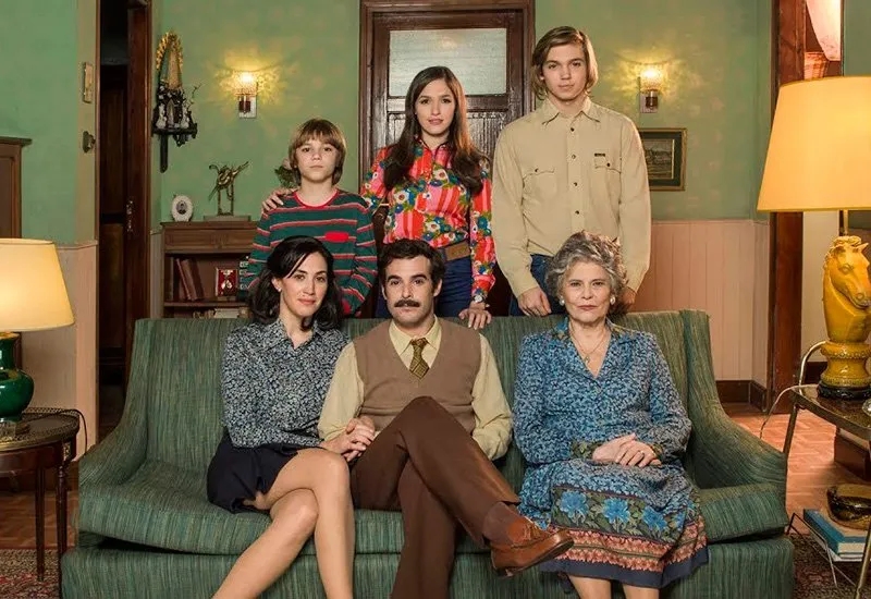 Seis personas posan en una sala de estar, dos adultos sentados en un sofá, niños detrás, todos en ropa casual de estilo retro