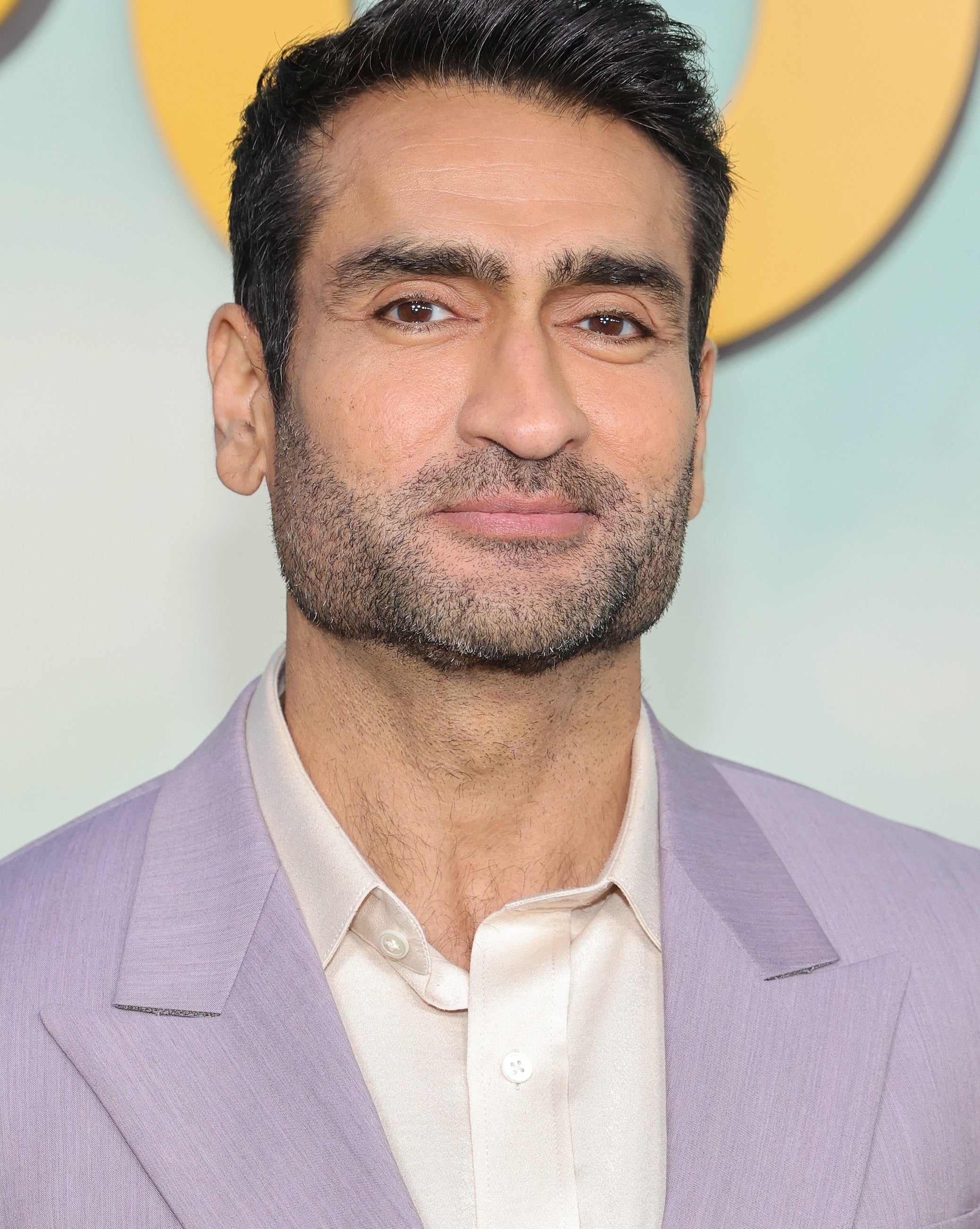 Kumail Nanjian wearing a light-colored suit jacket over a shirt poses at a formal event