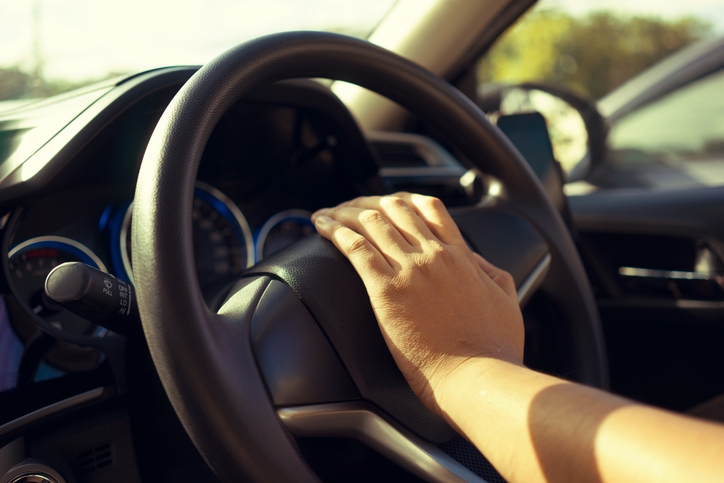 Person pressing a car horn with their hand on the steering wheel, sunlight illuminating the dashboard