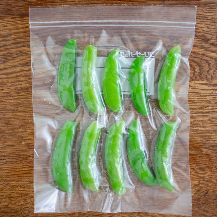 ジッパー付き袋に入った9本のスナップエンドウが木製のテーブルに置かれている。
