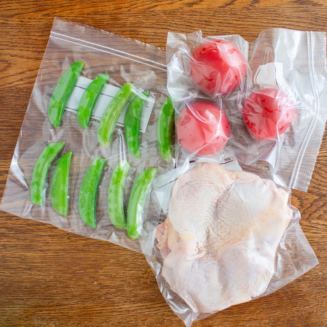 真空パックされたエンドウ豆、トマト、鶏肉が木のテーブルの上に配置されている。