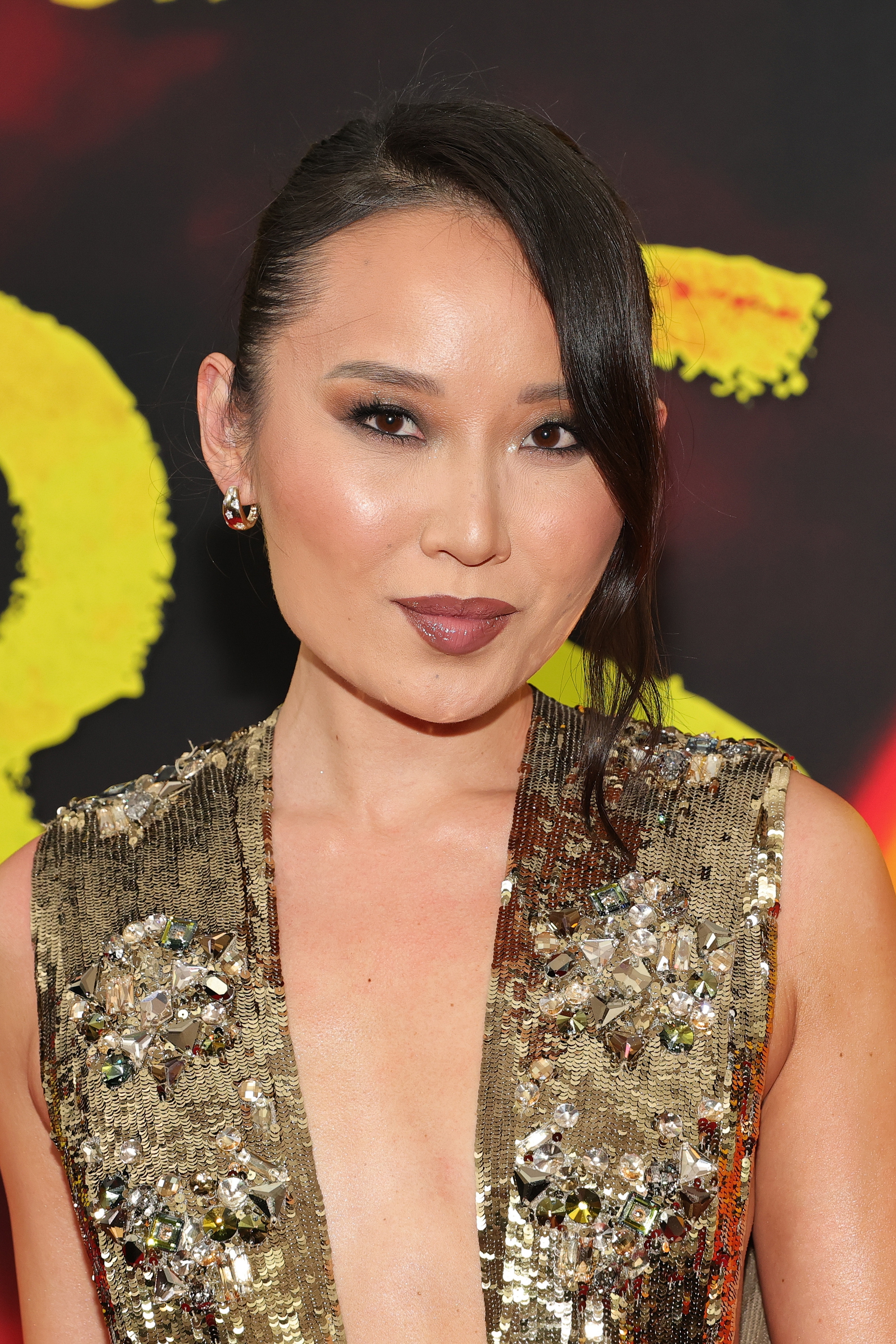 Woman on red carpet wearing a sequined, sleeveless dress with a deep neckline, hair styled in a side part