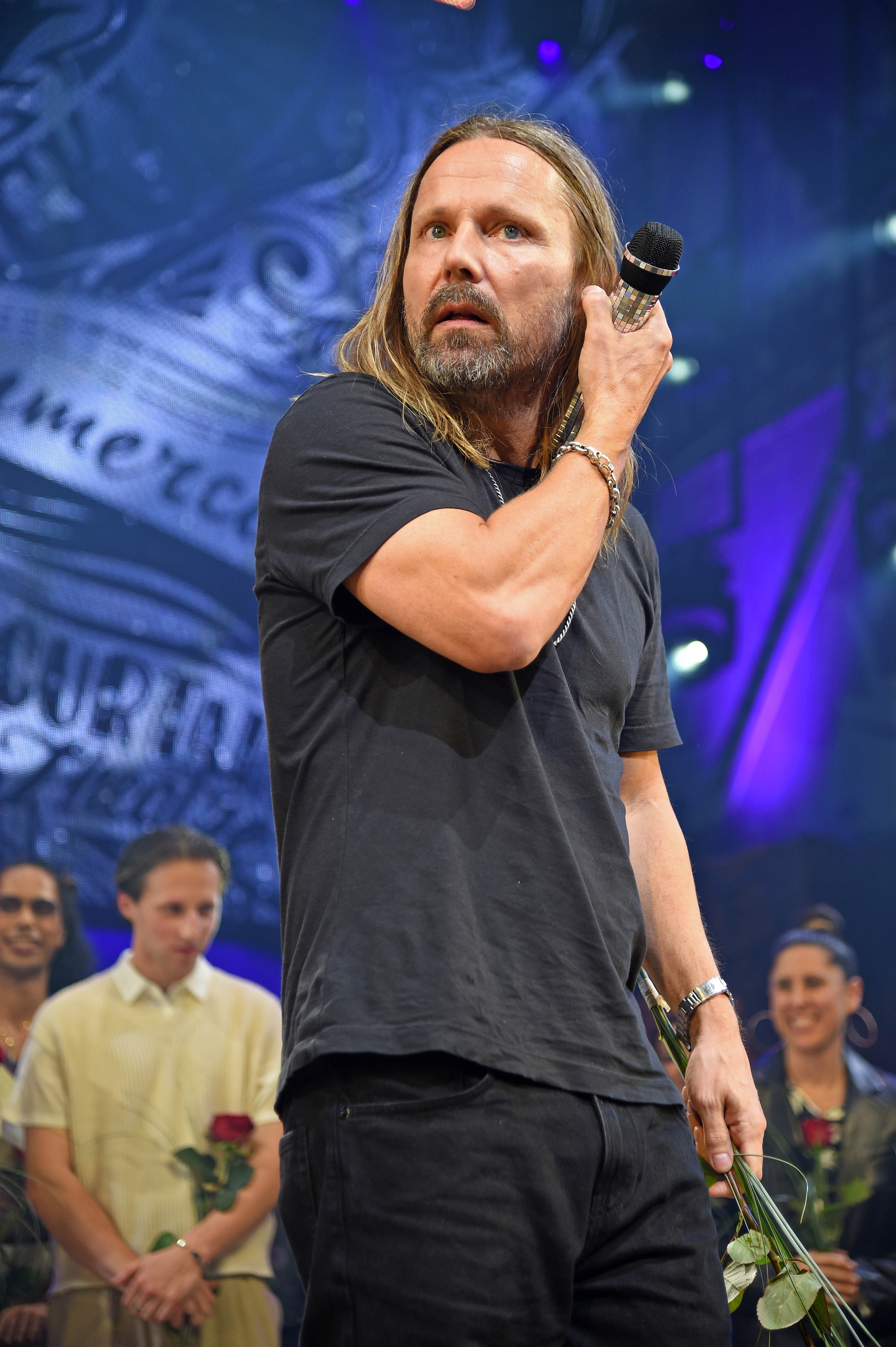 Max Martin stands on stage holding flowers, while others behind him also hold flowers