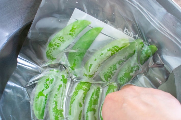 手が冷水に入れたジップロック袋の中の緑のピーマンを触っている様子。
