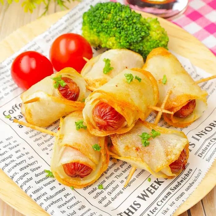 新聞紙の上に盛り付けられたソーセージ入りの焼き料理。横にトマトとブロッコリーが添えられている。