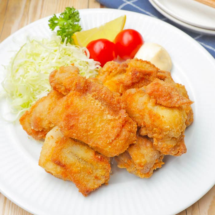 フライドチキン、キャベツ、トマト、レモンが白いプレートに盛り付けられています。