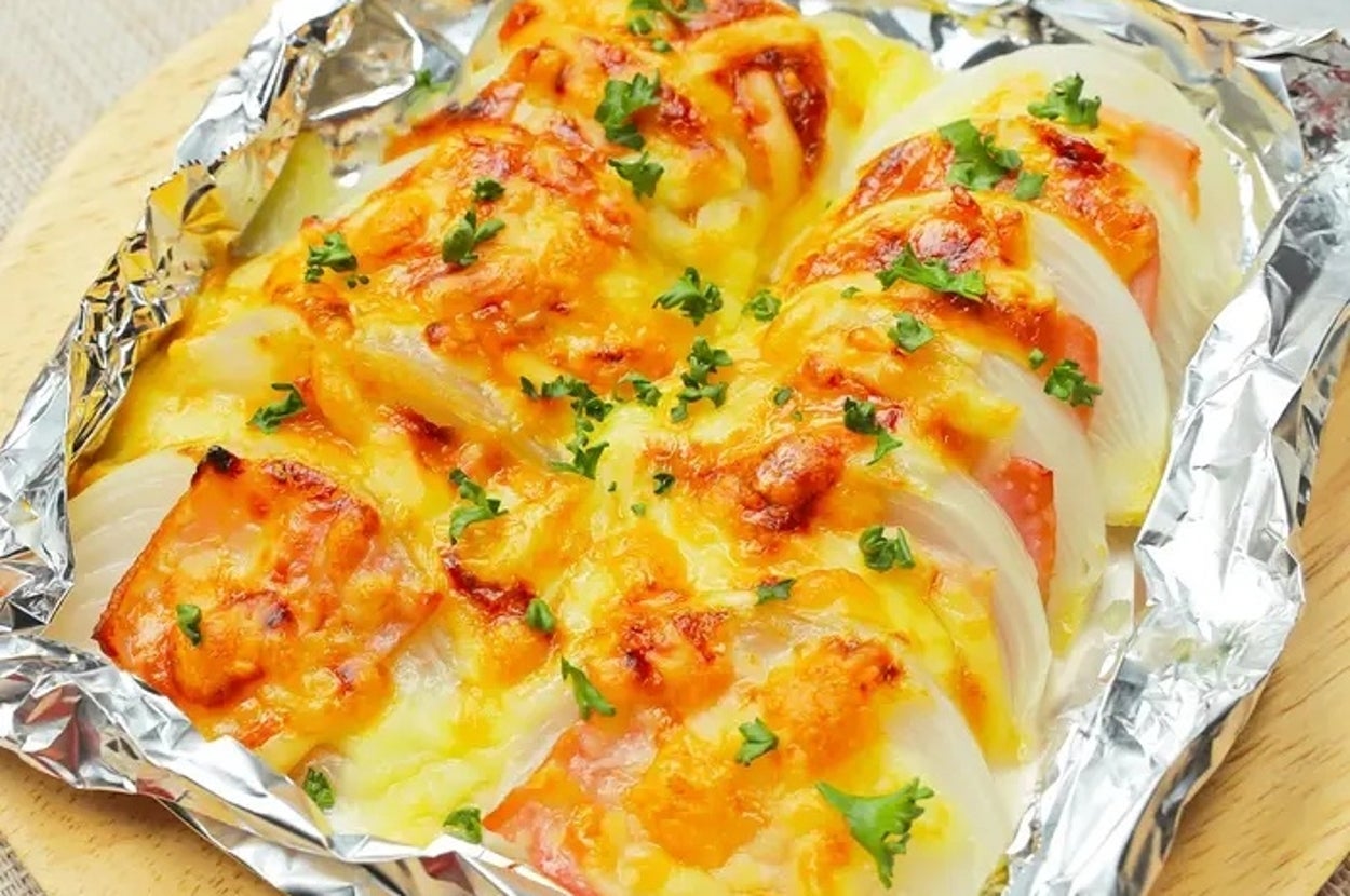 ホイルに包まれたチーズとハーブで焼かれた玉ねぎとトマトの料理。