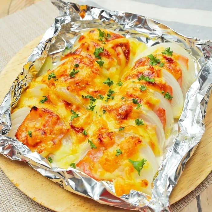 ホイルに包まれたチーズとハーブで焼かれた玉ねぎとトマトの料理。