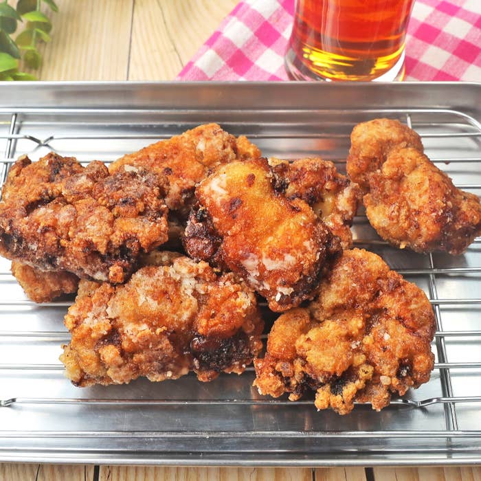金網のトレイにのせられた複数の揚げた鶏肉の唐揚げ。背景に飲み物が見える。