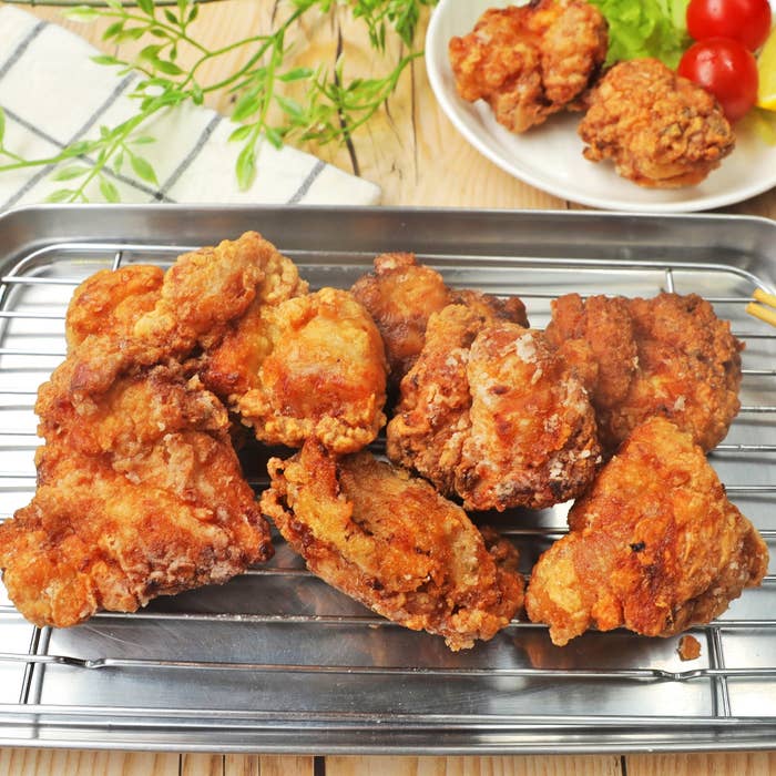 揚げたての唐揚げがトレーに並んでいる。後ろに野菜と唐揚げのある皿が置かれている。