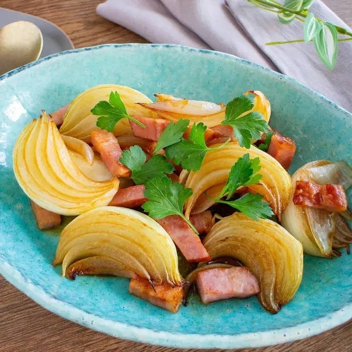 玉ねぎのスライスとベーコンが入った青い器に盛り付けられた料理。パセリが上に飾られている。