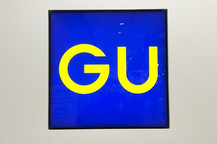 A square sign with the letters &ldquo;GU&rdquo; in bold, set against a plain background
