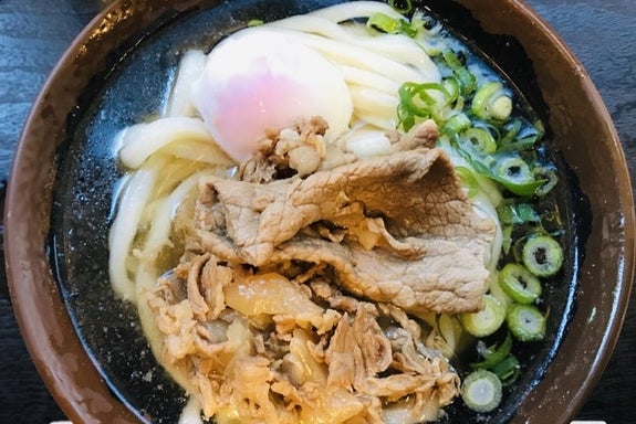 うどんに薄切りビーフ、温泉卵、ネギがのった料理。