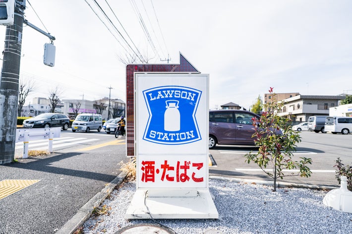 ローソンの看板がある道の風景。看板に酒・たばこの文字があり、通りを車が走っている。