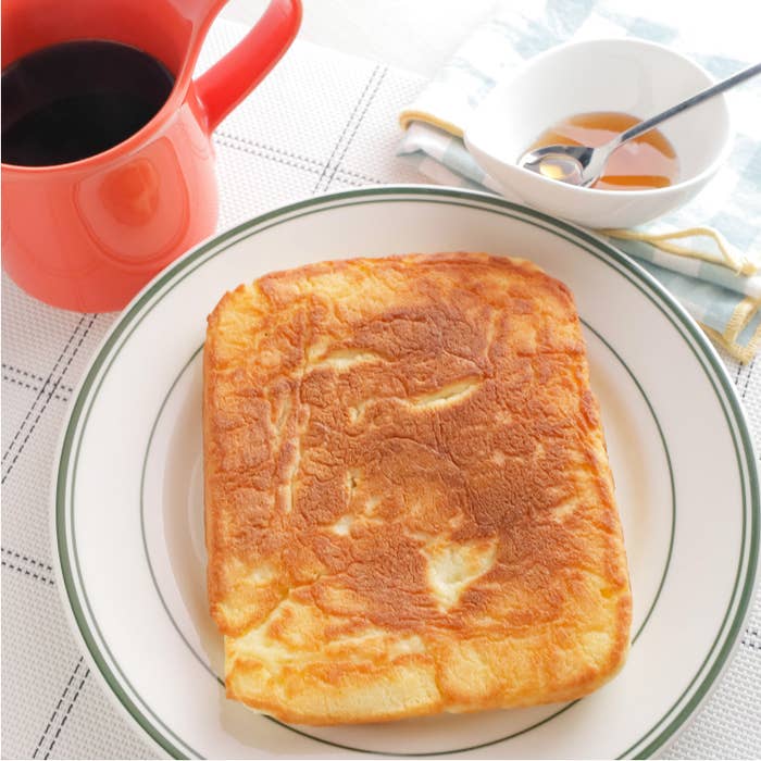 シンプルなパンケーキが皿に盛られ、横にはシロップとカップがあります。