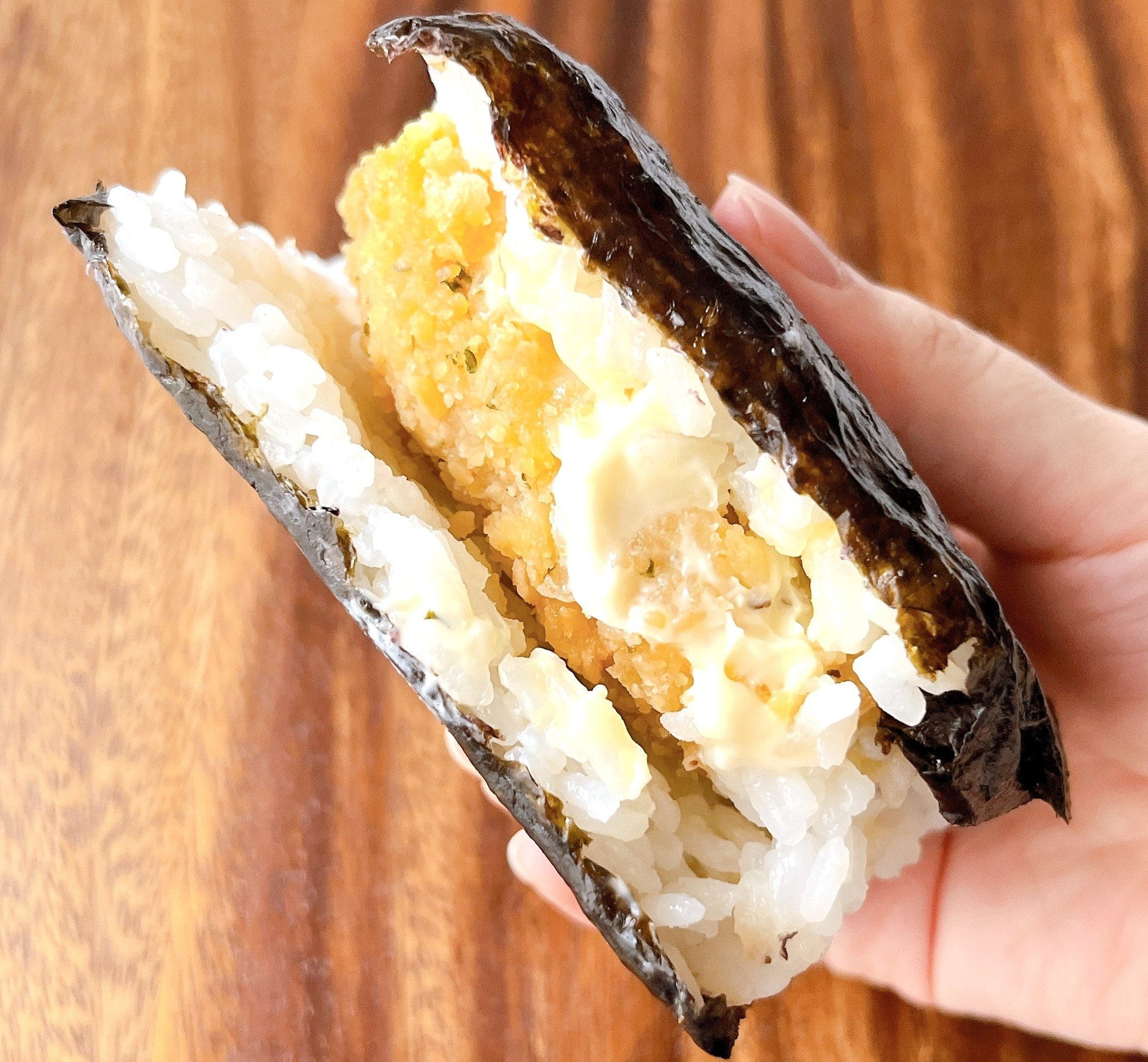 手に持たれた、ご飯で挟まれたチキンカツとマヨネーズの海苔サンドイッチ。