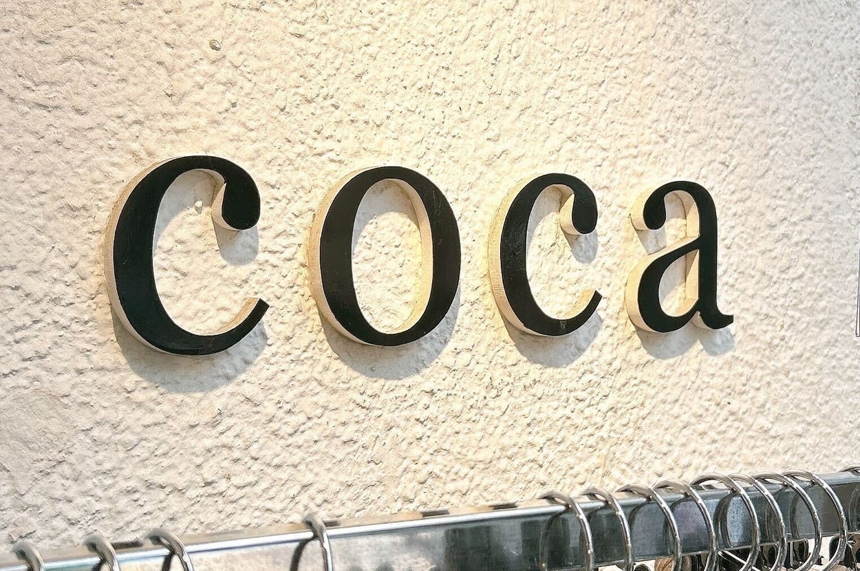 衣類を扱う店の壁に掛けられた「coca」の文字とラックにかかったハンガー。