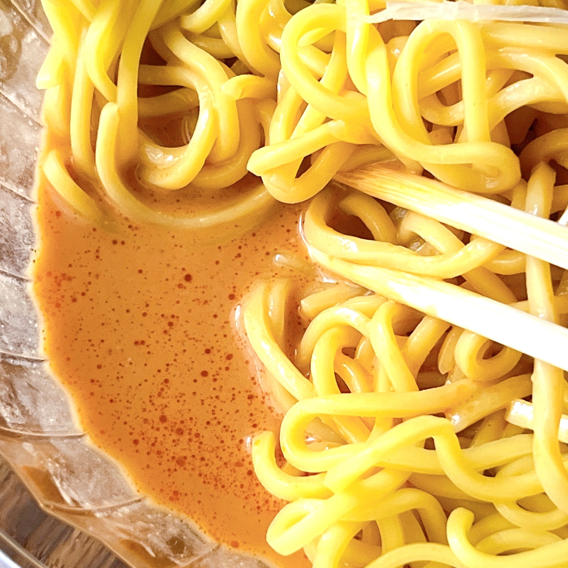 ラーメンの麺と濃厚なスープがガラスの器に入り、箸で持ち上げられている。