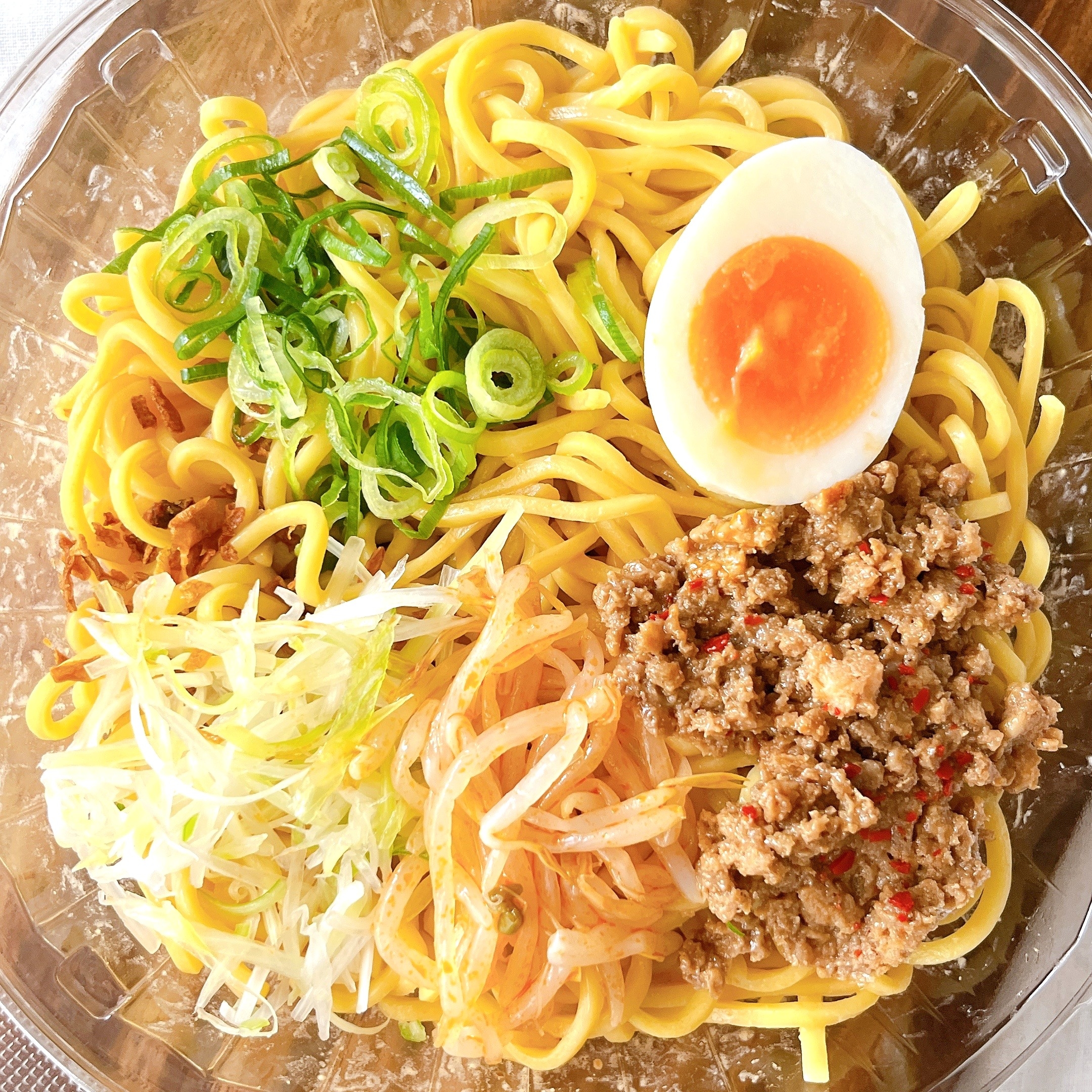 ラーメンボウルに麺、ひき肉、もやし、ネギ、ゆで卵が盛り付けられている。