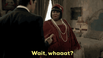 Person in vintage outfit with pearl necklaces reacts with surprise as another person gestures, over the text "Wait, whaaat?"