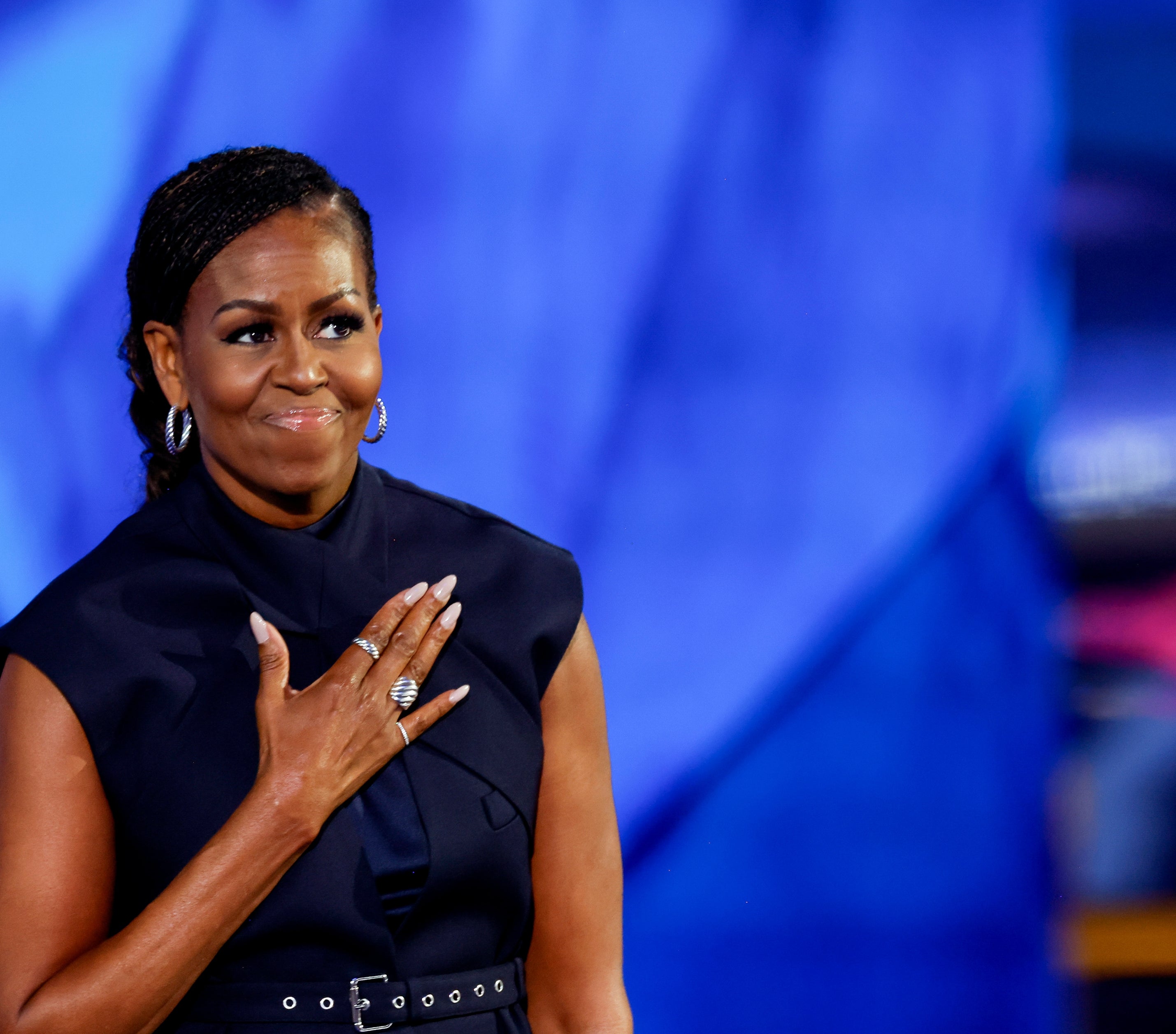 Michelle Obama on stage, smiling with one hand on her chest