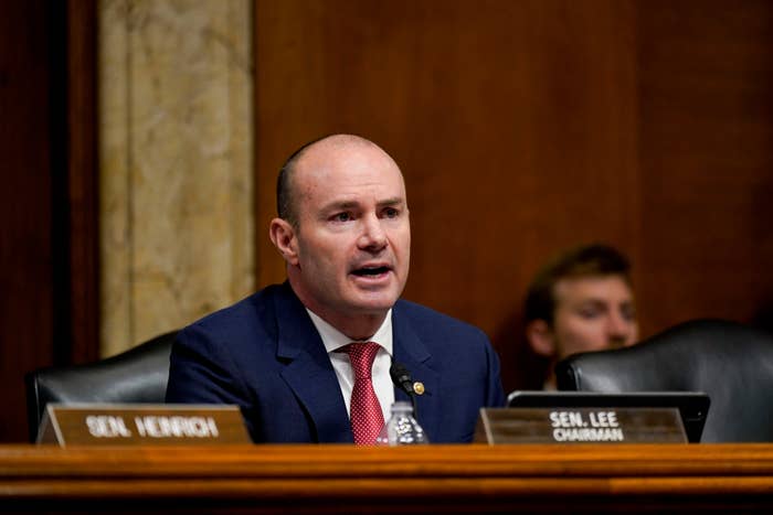 A man in a suit speaks at a government hearing with nameplates indicating his role as chairman