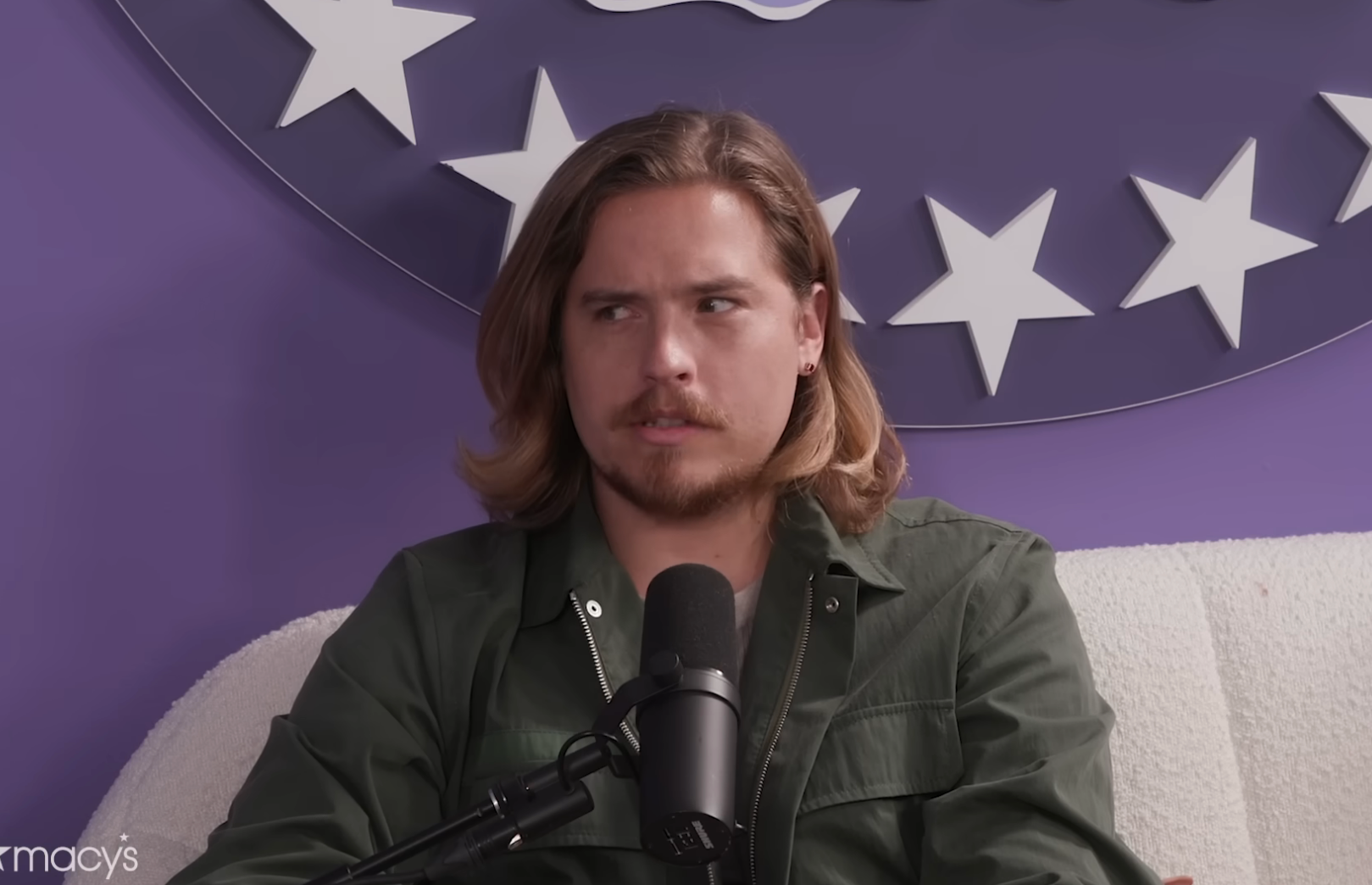Dylan Sprouse speaking into a microphone during an interview on a podcast set