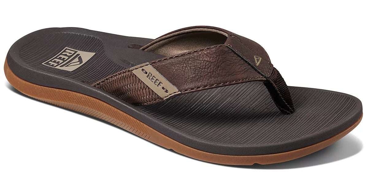 Sandal flip-flop kulit coklat dengan kaki bertekstur, tali tebal, dan logo merek, ideal untuk pakaian santai