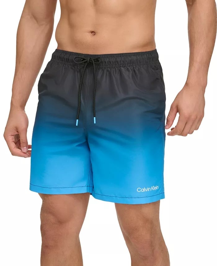 Pria yang mengenakan koper renang Calvin Klein dengan desain gradien biru, cocok untuk tamasya pantai atau kolam renang kasual