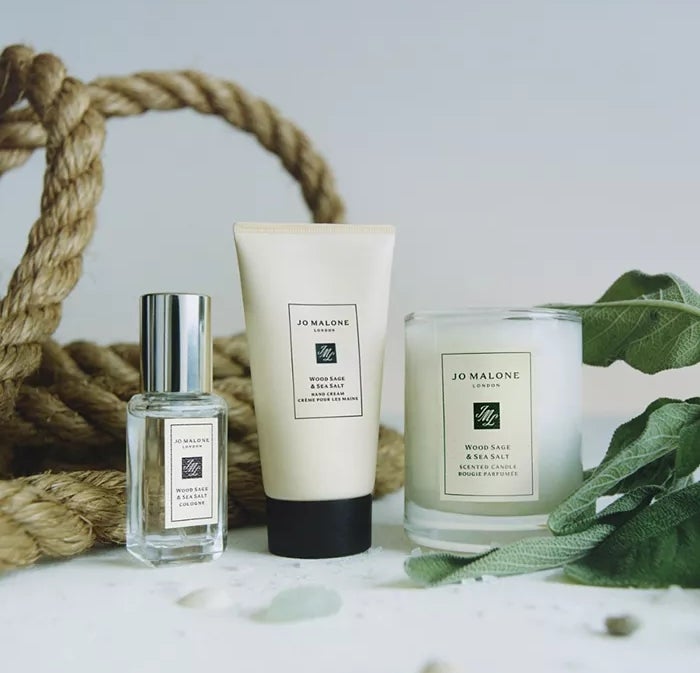 Jo Malone Wood Sage & amp; Koleksi garam laut, menampilkan cologne, krim tubuh, dan lilin, ditata dengan tali dan tanaman hijau untuk artikel belanja