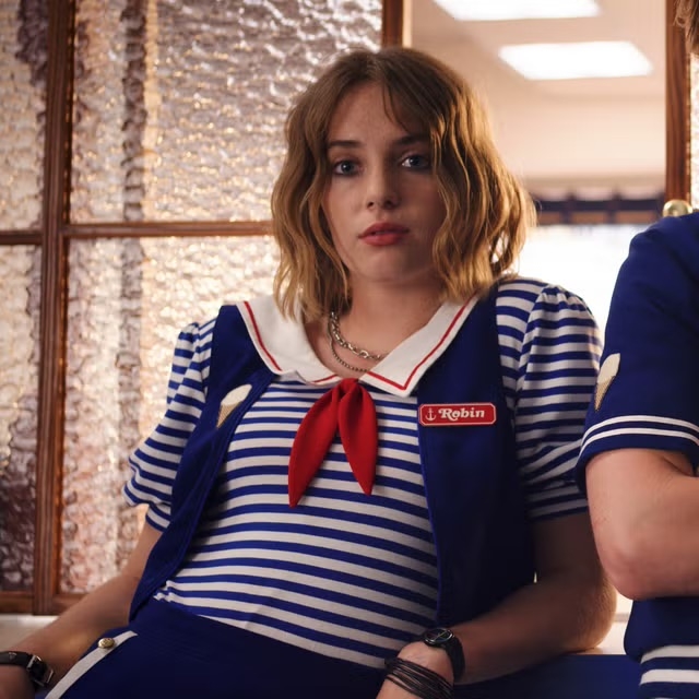 Persona con uniforme de marinero a rayas, pañuelo rojo y nombre "Robin", en un entorno interior, posiblemente set de película o serie