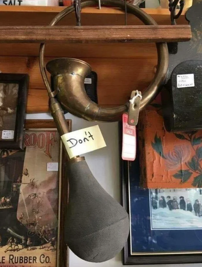Antique horn with a "Don’t" note attached, hanging on a wooden beam amidst vintage items, suggesting the horn is not to be used