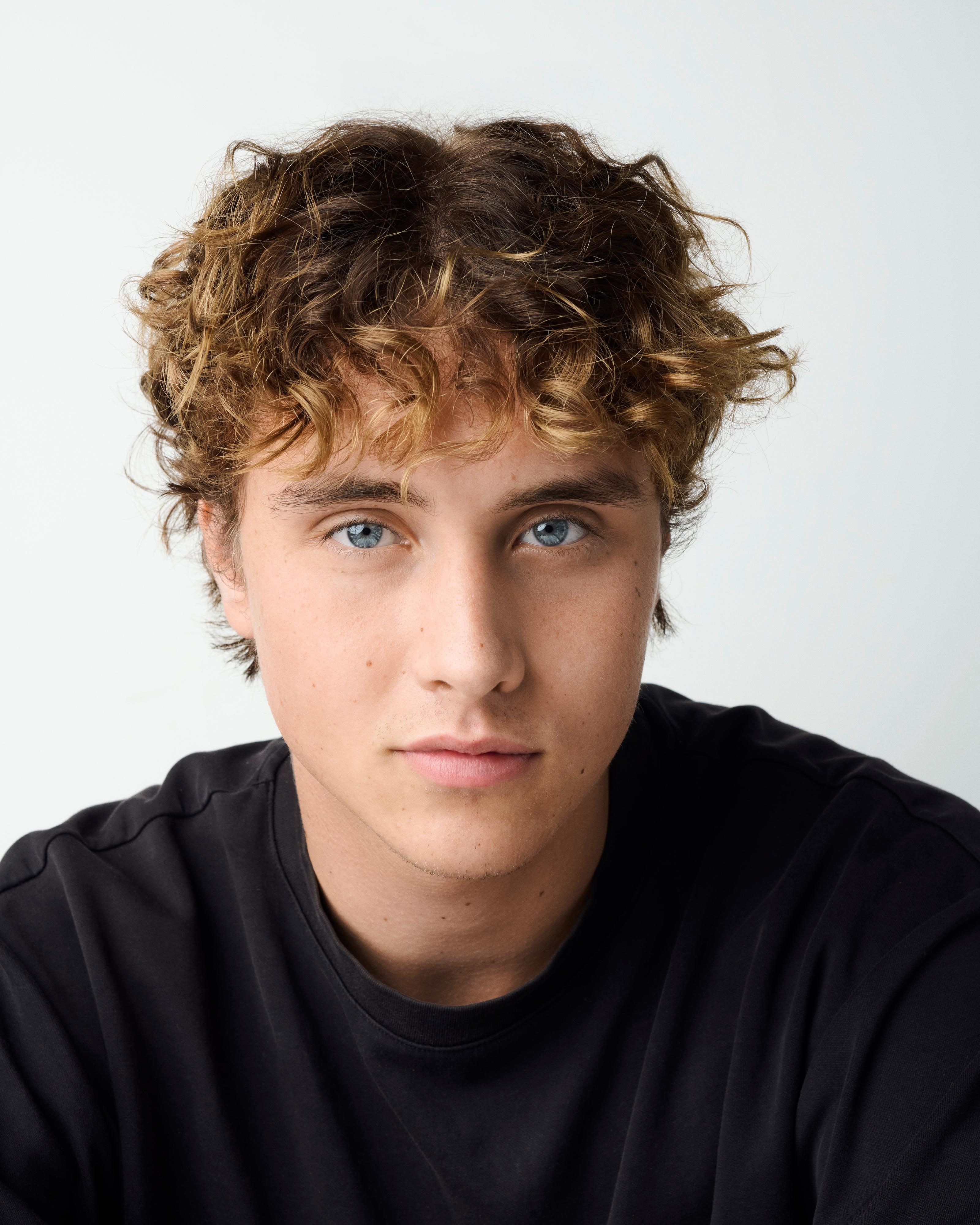 Persona joven con cabello rizado y expresión neutral, lleva una camiseta casual