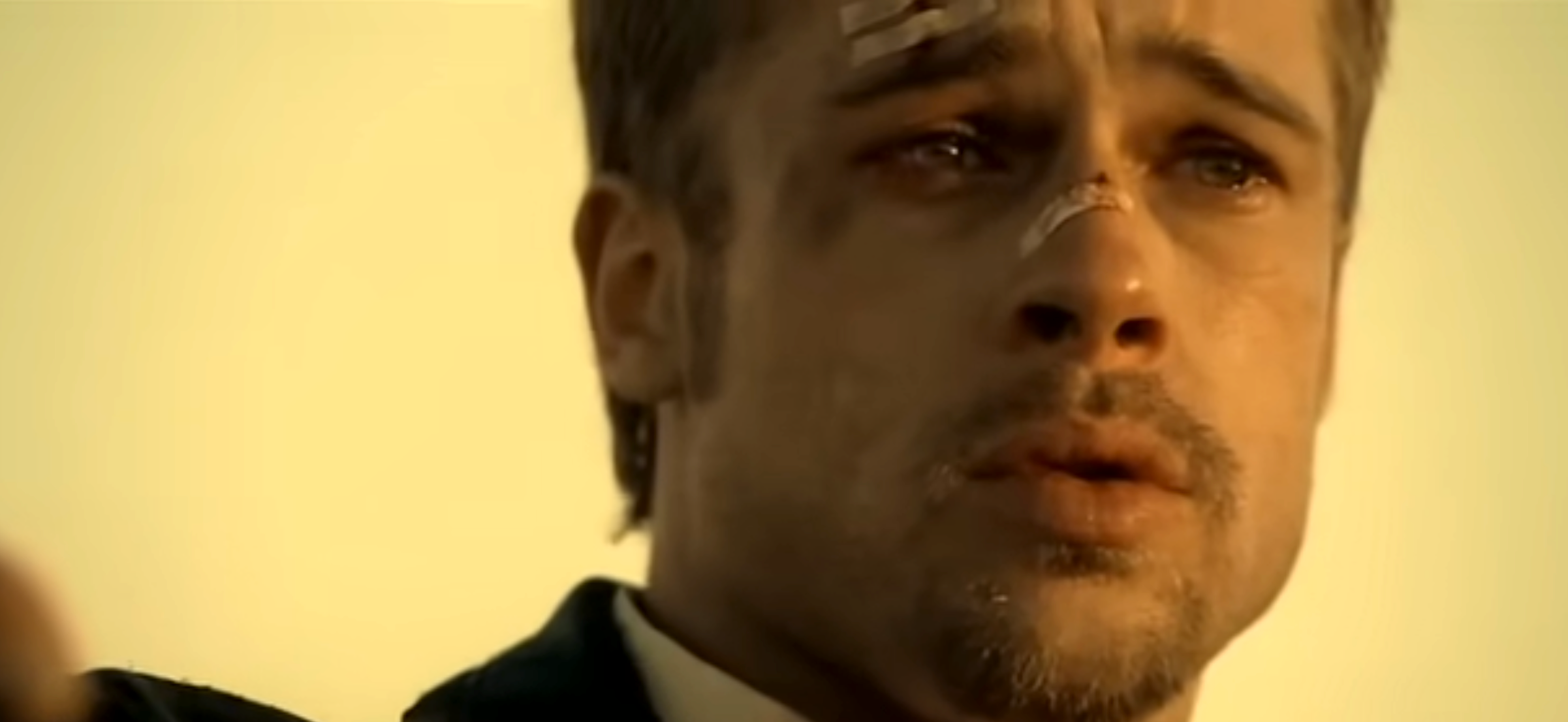 A man with facial injuries looks distressed, his eyes filled with emotion. He's in a tense moment, possibly from a dramatic scene in a film